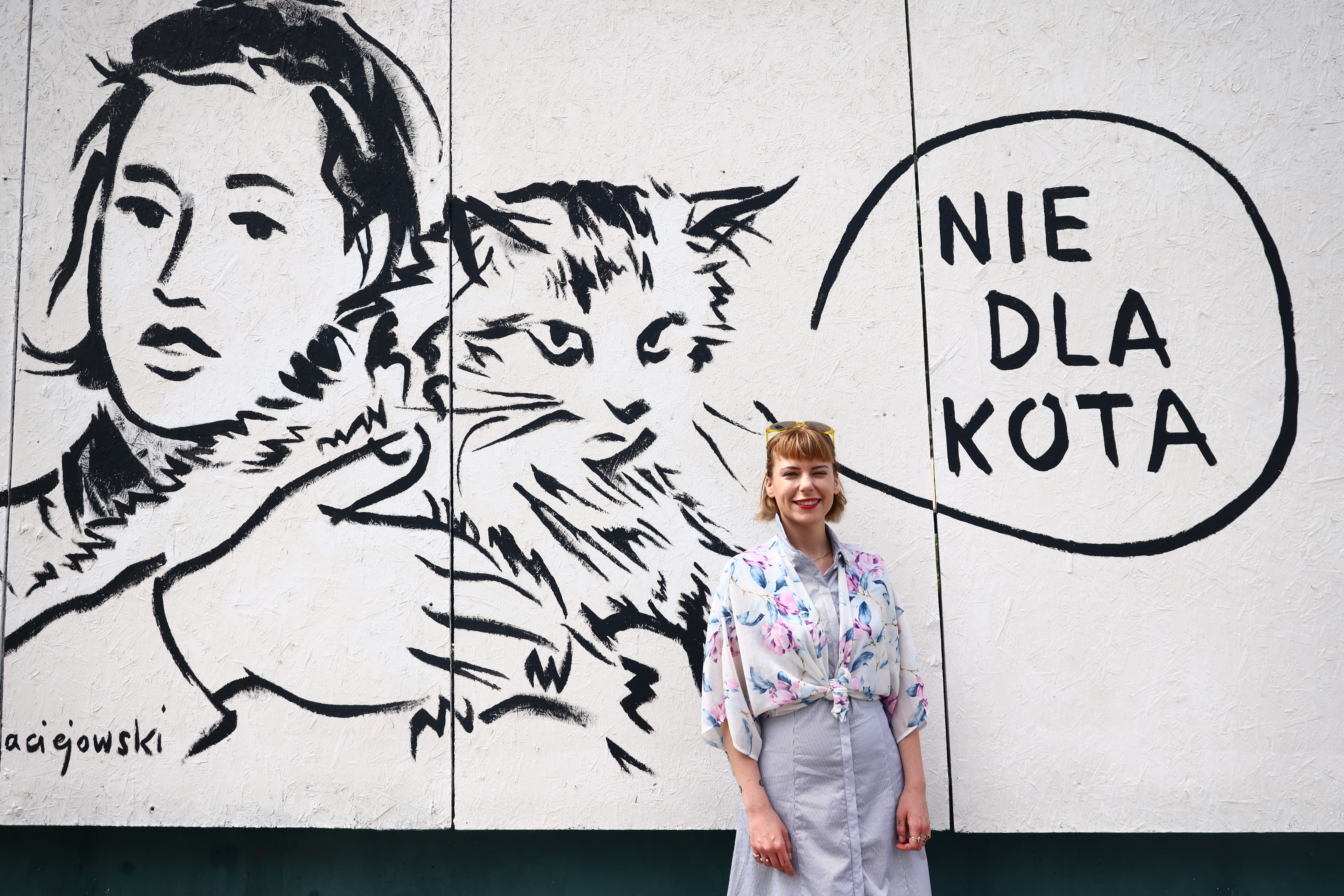 Czarno-biały mural z cytatem: ,,Nie dla kota". Przechodnie chętnie fotografują się na jego tle - tak jak ta młoda dziewczyna.